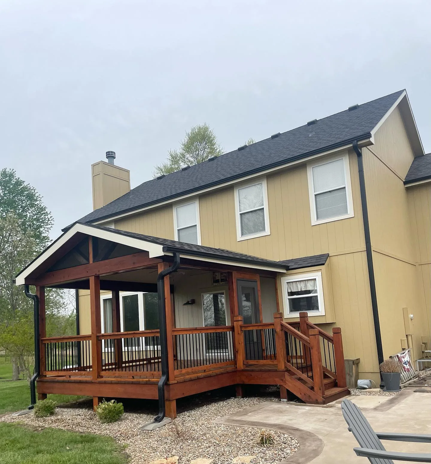 Covered porch and deck fully stained in warm cedar tones at a Lenexa, KS home — spring overcast sky