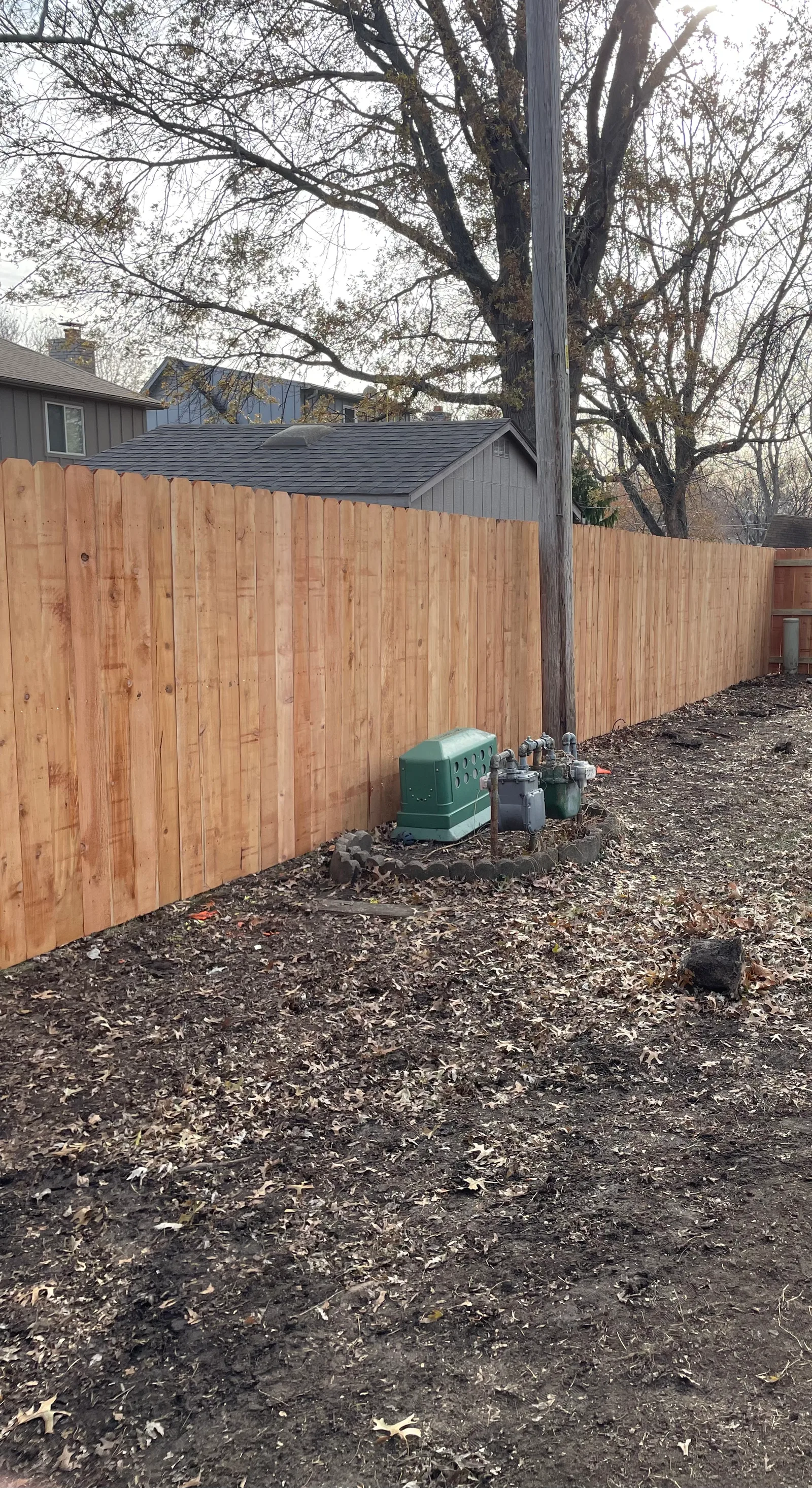New horizontal cedar privacy fence on a new construction lot in Smithville, MO — bare ground, utility marker visible